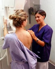 Fotografía de una mujer recibiendo un mamograma con la ayuda de una especialista en radiografía