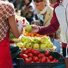 People are selecting fresh fruit and vegetables from a produce market while one customer is paying the vendor for a green apple.